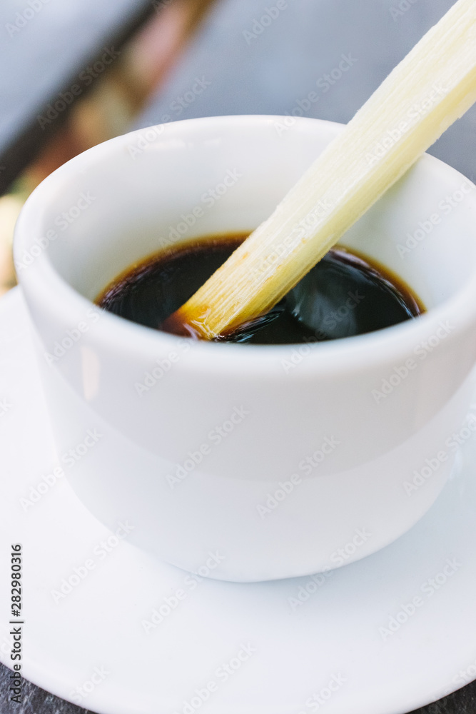 Close up of white mug of black coffee with fresh sugar cane swizzle stick on wood picnic table outdoors Close up of white mug of black coffee with fresh sugar cane swizzle stick on wood picnic table outdoors