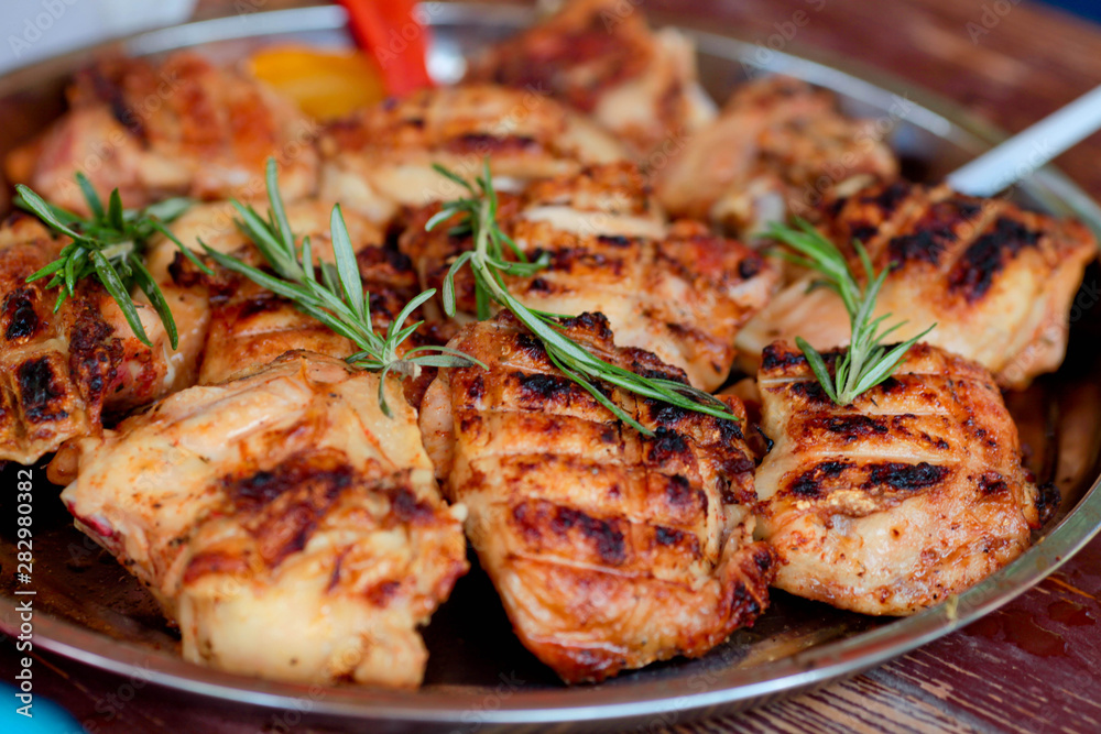 The chicken thighs fried on a barbecue close up, with rosemary branches on a tray. The chicken thighs fried on a barbecue close up, with rosemary branches on a tray.