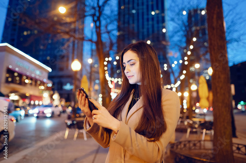 Beautiful girl in a evening city. Stylish brunette in a brown coat. Woman in a Chicago. Lady with a phone