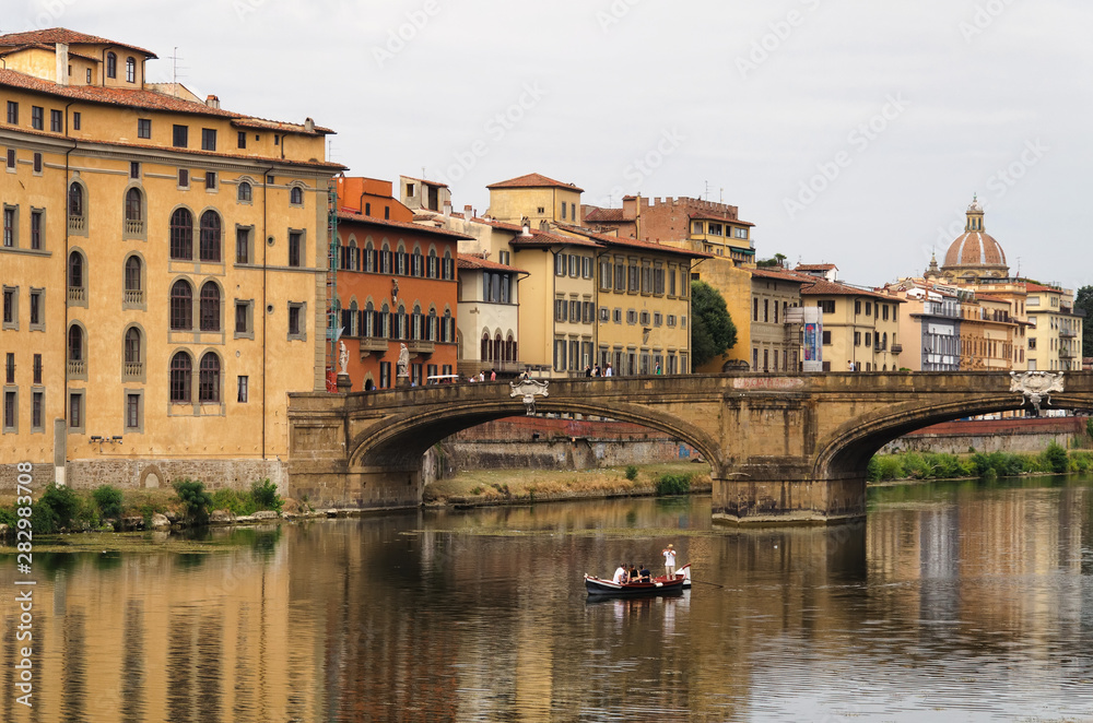 The river arno. Medieval bridge. Boat in the middle of the river. Cheap hotels in Florence, Tuscany, Italy.