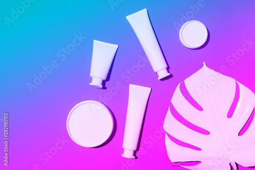 Cosmetics, skin care, beauty, body treatment concept. White cosmetic jar, tube, bottle and tropical monstera leaf over neon background. Top view. Flat lay. Mock-up.