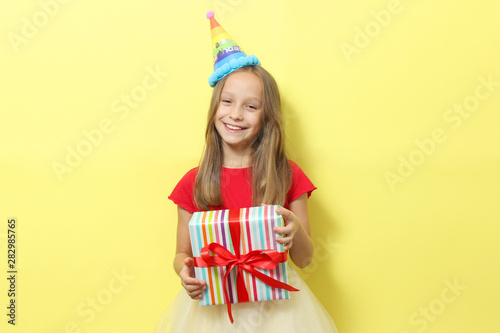 Portrait of a little girl in a festive cap and with a gift in her hands on a colored background. Birthday, presents, holiday