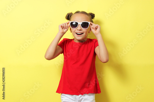 Little cheerful smiling girl in fashionable clothes on a colored background. Children's clothing, children's fashion