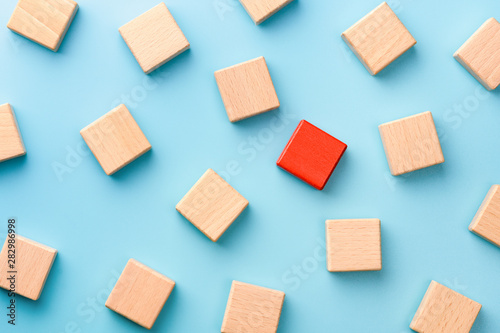 Red wooden block standing out from the group wooden blocks on blue background. Leadership, dissenting opinion, divergent views concepts photo