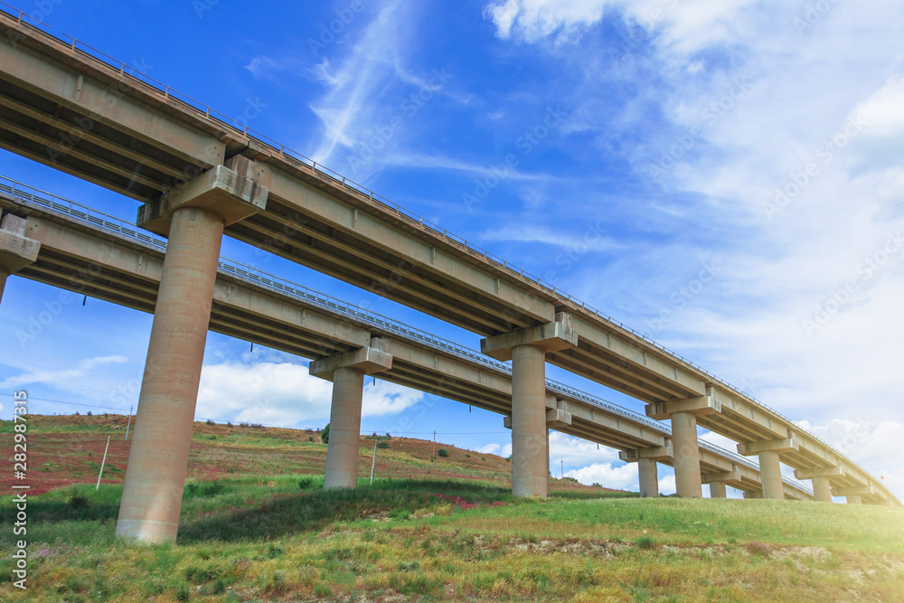 Two road turn highway bridge, viaduct supports in the valley among the green hills, transport infrastructure. Two road turn highway bridge, viaduct supports in the valley among the green hills, transport infrastructure.