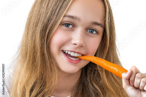 Beautiful smiling girl with long hair in a white shirt bites carrots isolated on white background