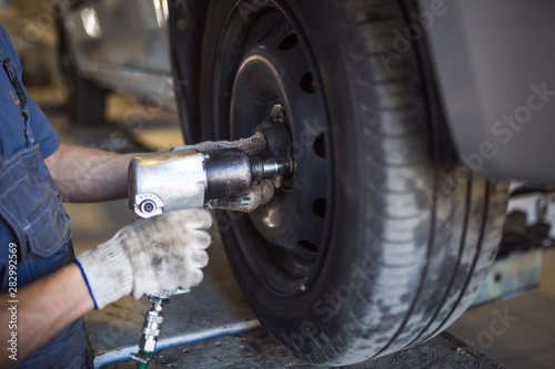 Car repair in the service station. Hands of a mechanic in overalls repairing the car on the lift without wheel, holding the tire and mechanical works.