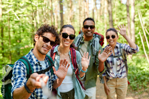 travel, tourism, hike and people concept - group of friends with backpacks taking picture by selfie stick and waving hands in forest © Syda Productions