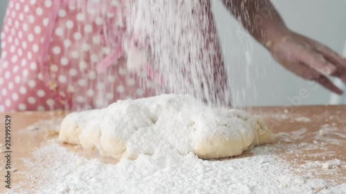 Girl with pink apron sprinkling flour on dogh, slow motion. photo