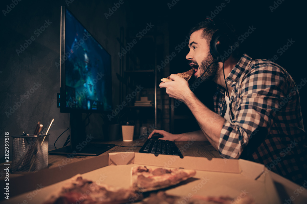 Close up side profile view photo he him his guy videogame headset microphone teammates concentrated look screen hand arm put pizza slice mouth wear casual plaid checkered shirt cafe table indoors Close up side profile view photo he him his guy videogame headset microphone teammates concentrated look screen hand arm put pizza slice mouth wear casual plaid checkered shirt cafe table indoors