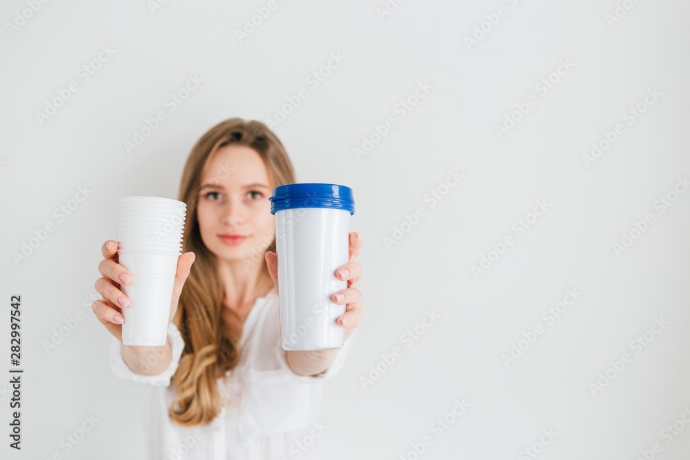 Girl holding a useful reusable glass and disposable plastic cups for comparison Girl holding a useful reusable glass and disposable plastic cups for comparison