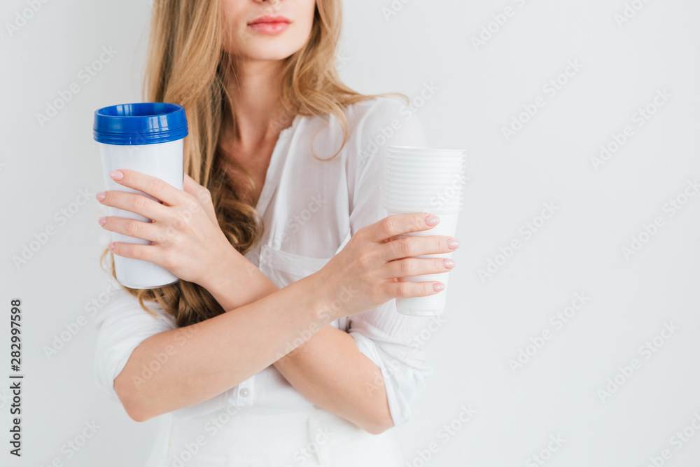 Girl holding a useful reusable glass and disposable plastic cups for comparison Girl holding a useful reusable glass and disposable plastic cups for comparison