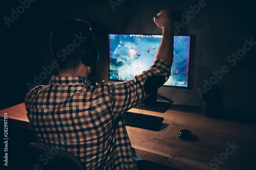 Close up back rear behind view photo he him his guy videogame talk headset microphone strategy raise fist hand arm hopeful speech team wear casual plaid checkered shirt internet cafe table indoors