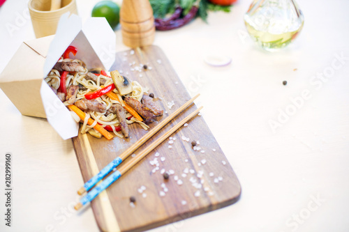 Wok. Noodles with vegetables and beef in take-out box on wooden table