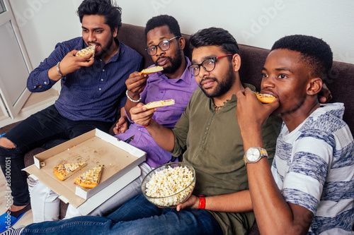 four african american males eating pizza at home party throwing popcorn into each other