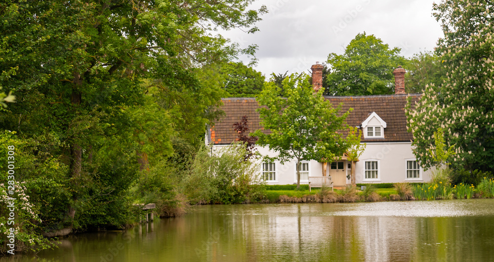 Fototapeta premium Traditional white cottage with its own tree lined lake, Norfolk, UK.