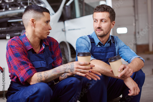 Two automechanics drink coffee at their lunch break.