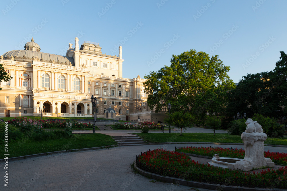 Naklejka premium Ukraine, Odessa, 13th of June 2019. Side view of the national academic opera building and the park with the sculpture fountain youth during a sunny day