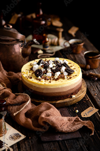 Fototapeta Naklejka Na Ścianę i Meble -  Beautiful still life with homemade delicious three chocolates cheese cake on wooden stand on rustic table
