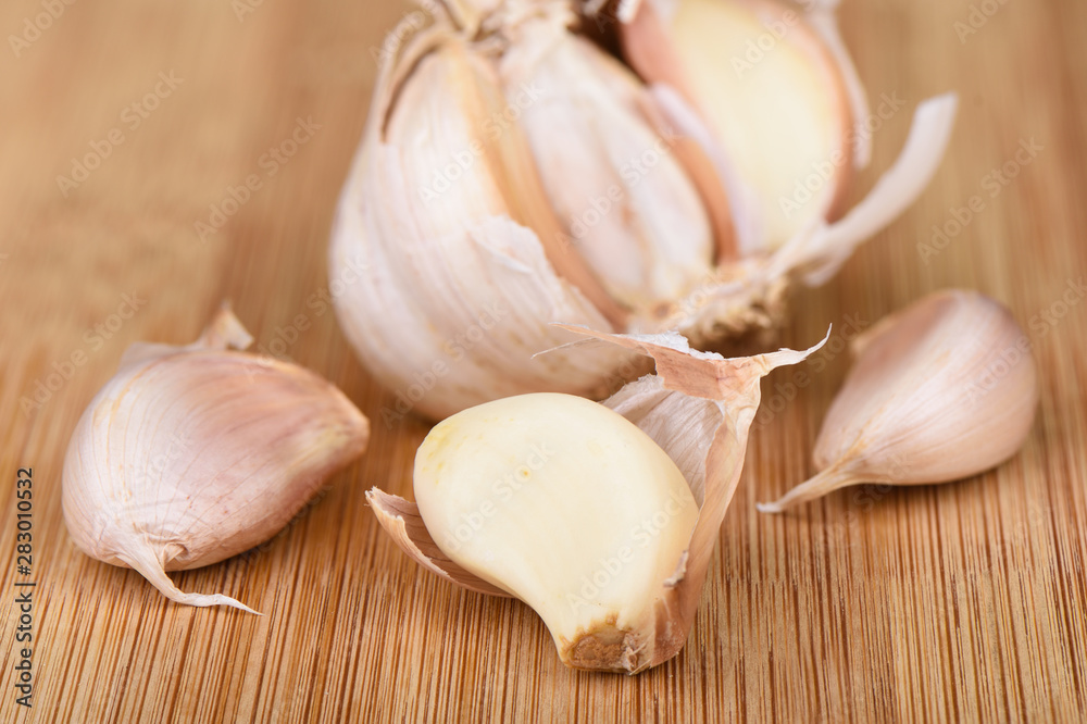 A head of garlic, several cloves of unpeeled garlic and a clove peeled on a wooden background. A head of garlic, several cloves of unpeeled garlic and a clove peeled on a wooden background.