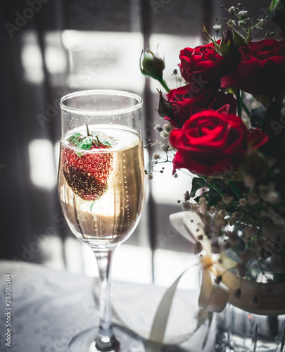 Glass of champagne with strawberry and red roses