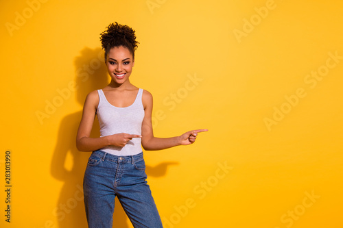 Close up photo cute beautiful she her dark skin lady toothy summer sale discount low prices indicate fingers empty space advising buy buyer wear casual jeans denim tank-top isolated yellow background