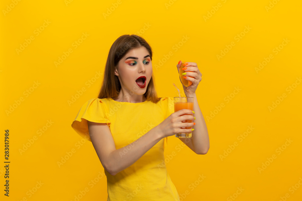 Close-up portrait of a beautiful young girl squashing orange juice into glass isolated over yellow background. Close-up portrait of a beautiful young girl squashing orange juice into glass isolated over yellow background.