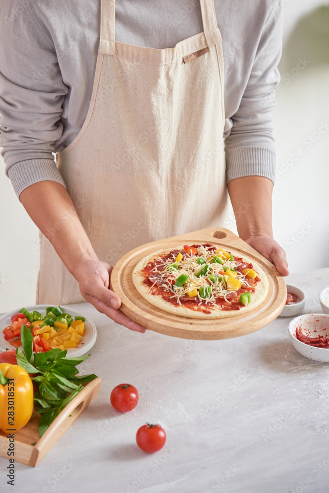 Raw pizza with ingredients in the background