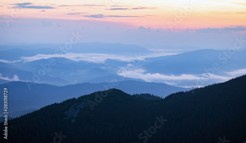mountain valley covered with fog in the orange and blue twilight light. mountain silhouette