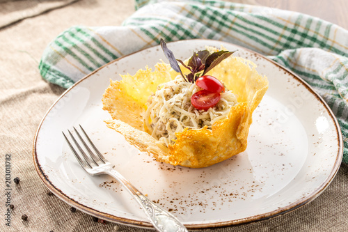 Fresh salad with cheese and walnut in edible melted cheese bowl on grey tablecloth