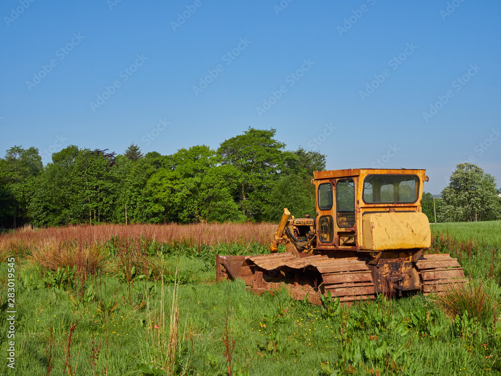 Obraz premium An Old Bulldozer in a Farm Field near Letham in Angus, Scotland, Its yellow Cabin rusted with age. Going nowhere.