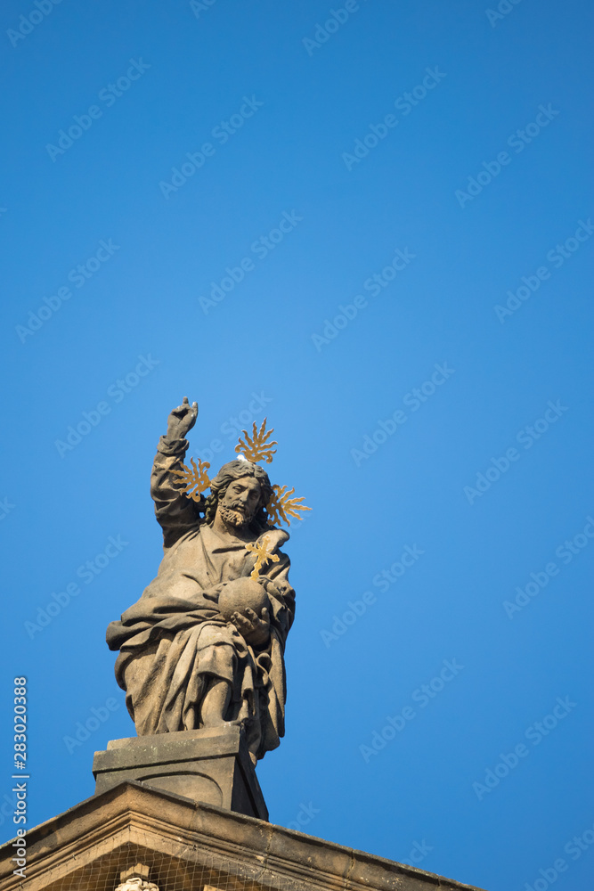 Statue on roof of St. Francis of Assisi church in Prague with blue sky in background