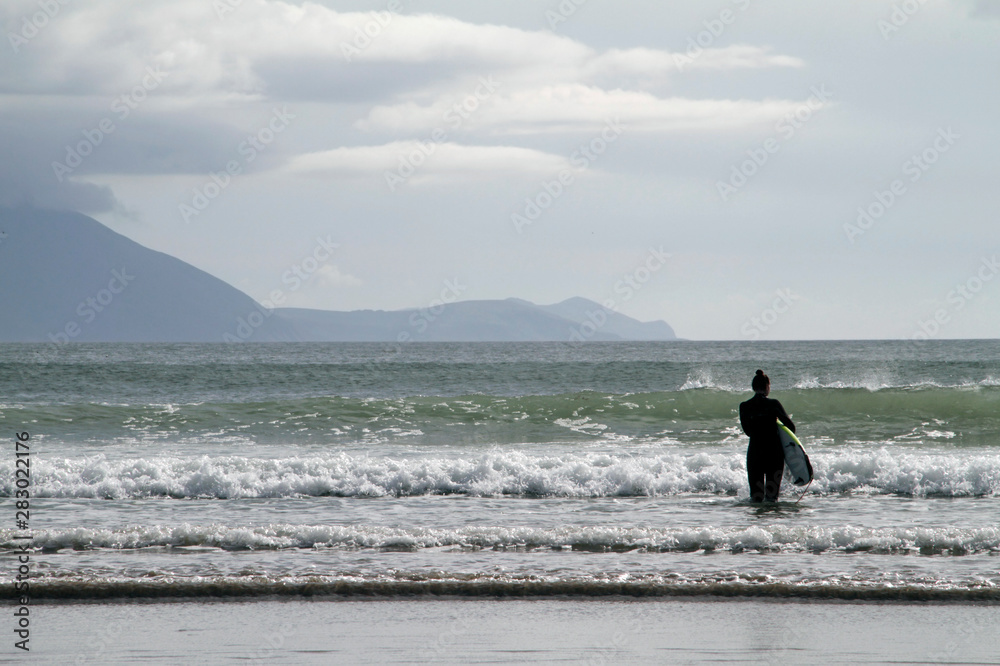 Surfer girl looking out for the perfect wave at the rugged coast of Inch Beach, Ireland