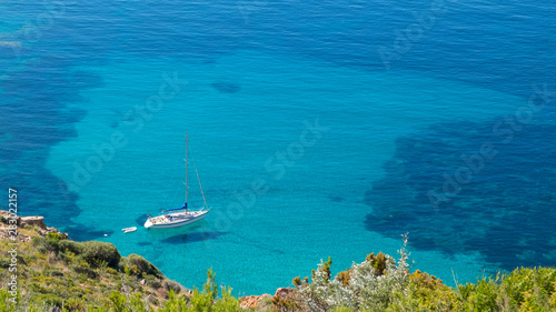 Segelschiff, das im türkisfarbenen Meer in einer Bucht von Korsika vor Anker liegt.