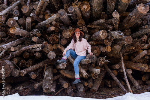 young beautiful woman sitting on wood trunks and smiling. Winter season Outdoors and lifestyle
