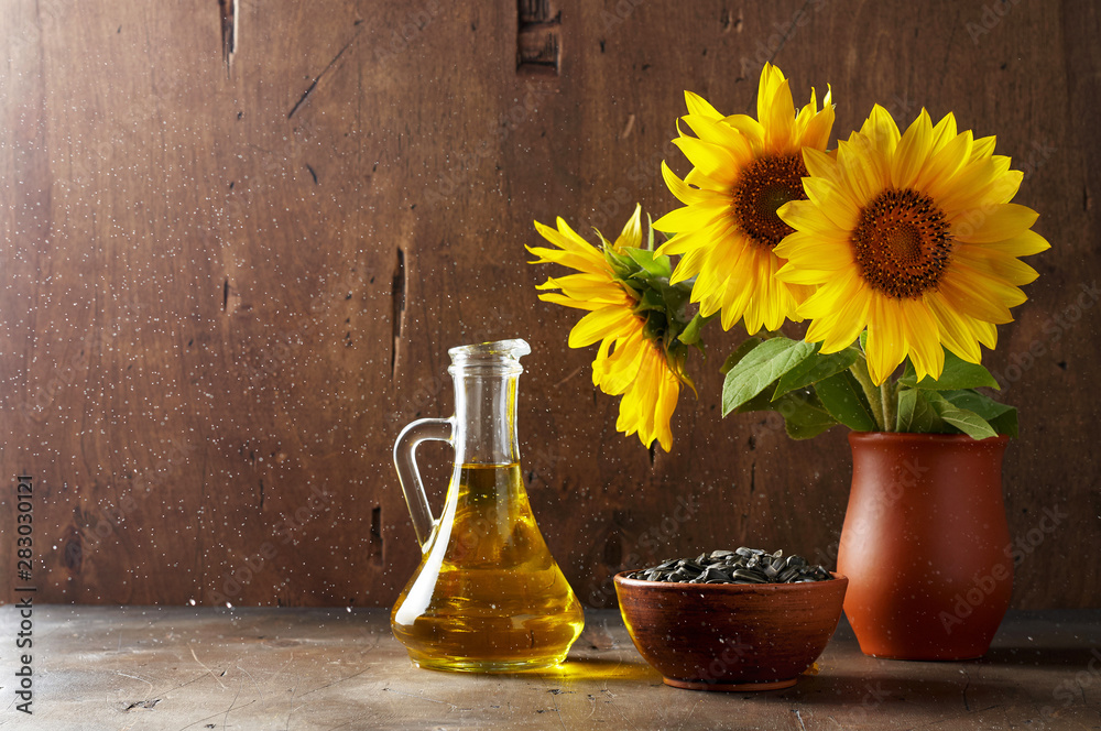 Still life of glass bottle with sunflower oil, seeds and flowers in ceramic vase
