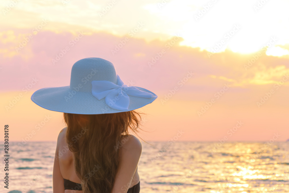 Girl in a hat, back view. Sunrise on the sea. The concept of harmony, tranquility, beauty.