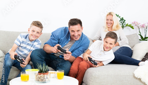 Happy young family playing videogame console on TV. Spending quality leisure time with children and family concept. Gaming consoles are generic and debranded. photo