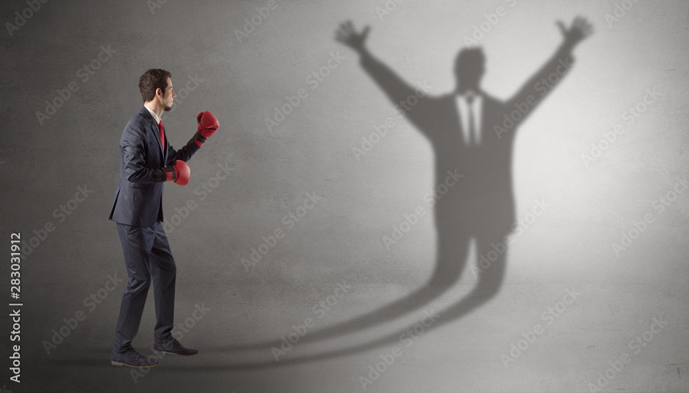 Fototapeta premium Businessman with boxing gloves fighting with disarmed businessman shadow