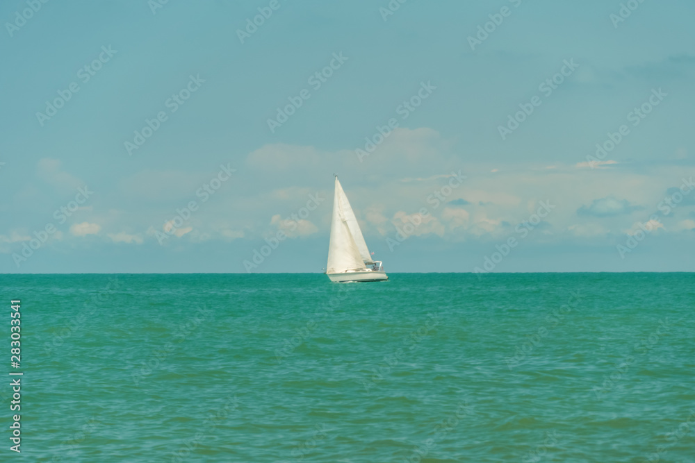 White sailing yacht in the black sea against the sky with clouds in sunny weather