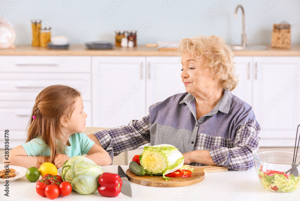 Cute little girl with grandmother preparing vegetable salad in kitchen Cute little girl with grandmother preparing vegetable salad in kitchen