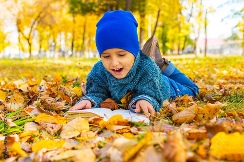 cheerful boy lying on yellow leaves with a book