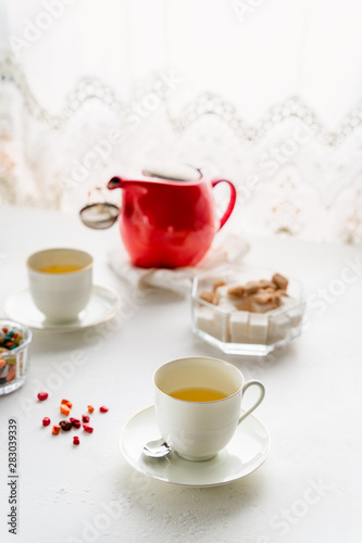 Red tea pot, two white tea cups, sugar bowl on a table by window