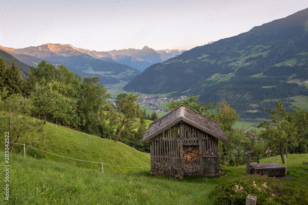 Classic view in the european Alps: storage cabin with a valley and surrounding mountains as background. Famous alpenglow on top of distant mountains.