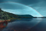 Rainbow over the river with reflection in the water against the cloudy sky