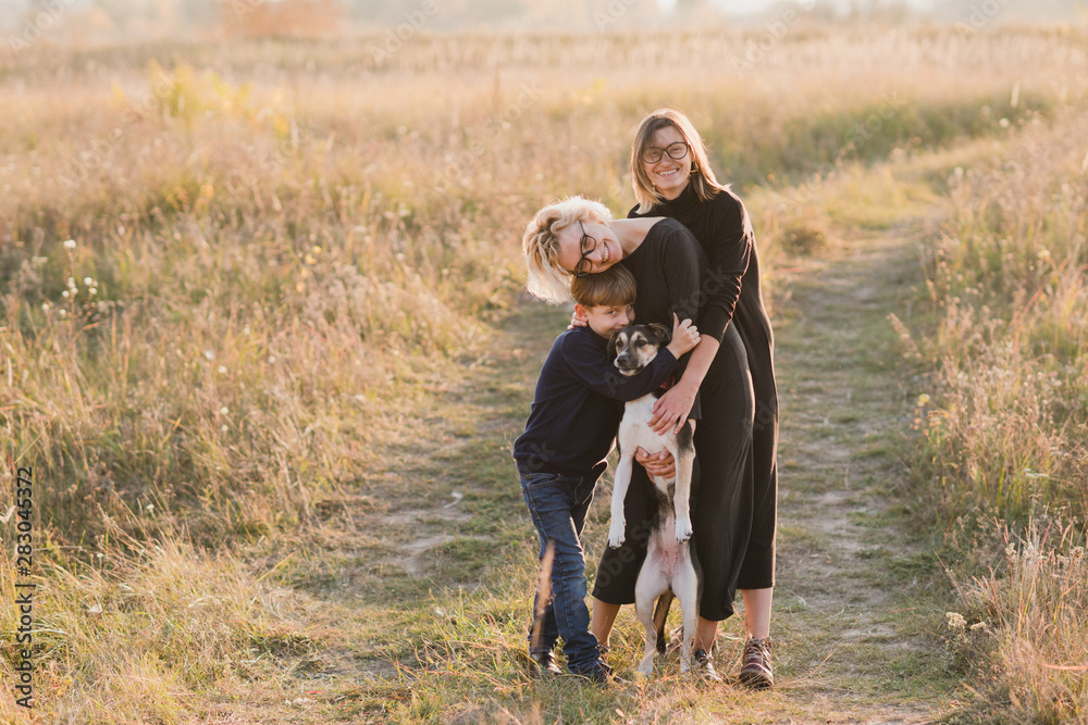 Samesex caucasian lesbian family with a child and a dog walking outdoors on the background of beautiful nature. Mothers having fun with their son.