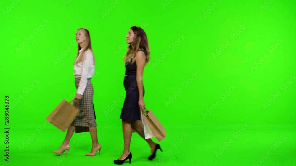 Two relaxed fashionable shoppers walk from side to side, looking at the stores, over green screen, 2 takes. Two relaxed fashionable shoppers walk from side to side, looking at the stores, over green screen, 2 takes.