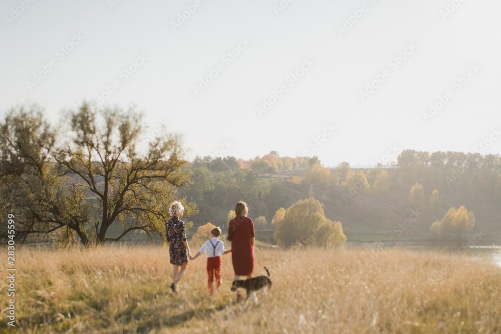 Samesex caucasian lesbian family with a child and a dog walking outdoors on the background of beautiful nature. Mothers having fun with their son.