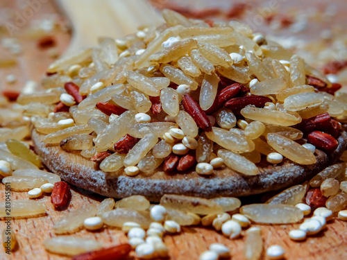 Mix red rice, complete rice, quinoa uncooked on wooden spoon and wooden surface 