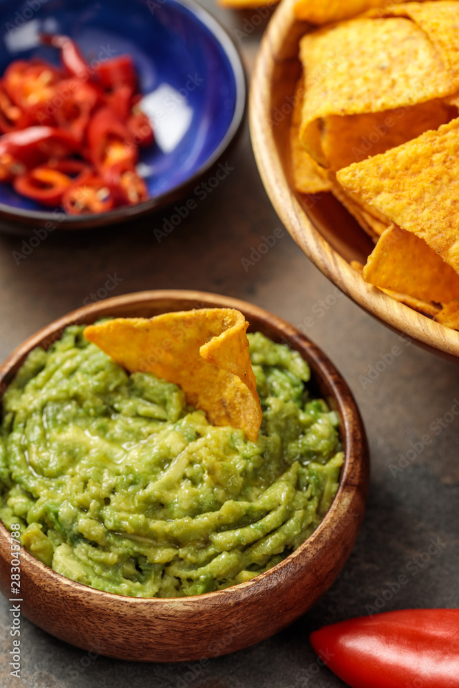 selective focus of Mexican nachos with guacamole and chili peppers on stone table